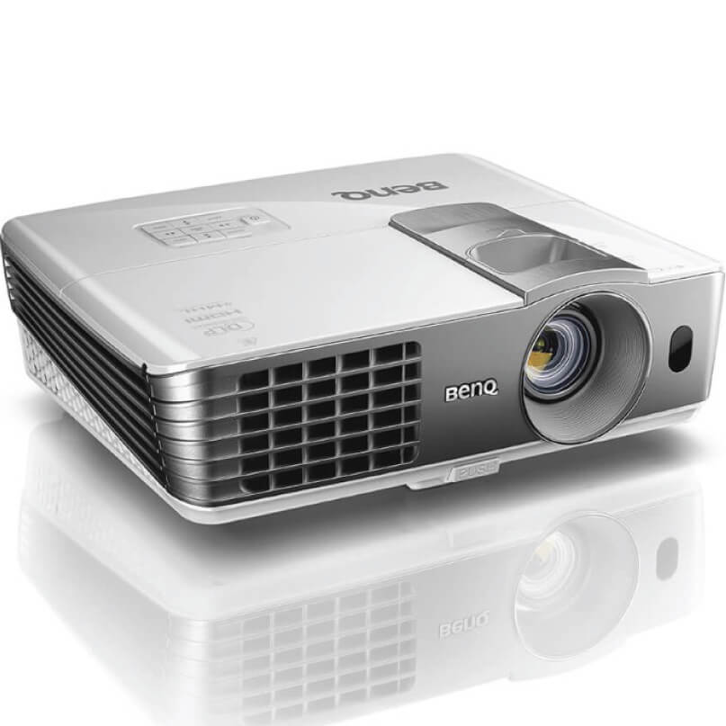 Benq W1070+ Home Video Projector The benq w1070+ home video projector, featuring a silver finish with a visible lens, vented sides, and top-mounted control buttons, is placed on a white surface.