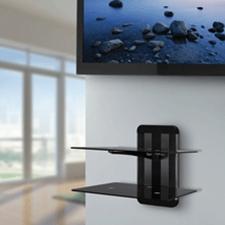 An AVF ZMS1200 Unimax Any Wall TV AV Accessory Shelving unit with two tiers of black glass is mounted on the wall below a flat-screen TV in a bright, modern room.