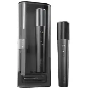 Ikarao MicBox Pro, A dark gray Ikarao wireless microphone with a silver grille stands beside its tall, translucent black charging case, which contains another identical microphone and a receiver.