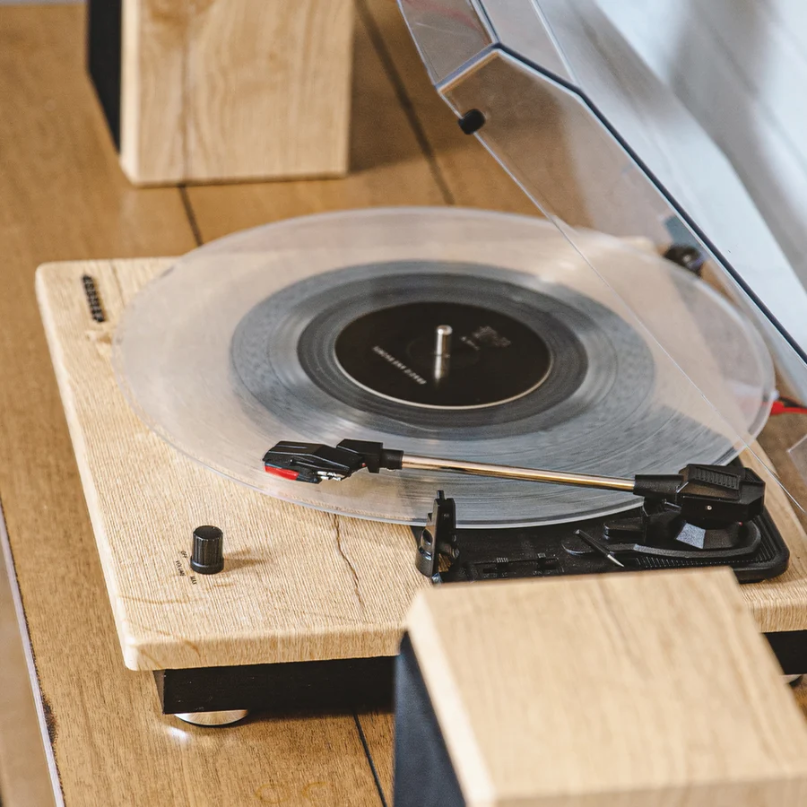 Crosley Brio Record Player Shelf System With Speakers A crosley brio record player shelf system with speakers spins a clear vinyl record on its wooden turntable, featuring a transparent dust cover and resting on a wooden surface.